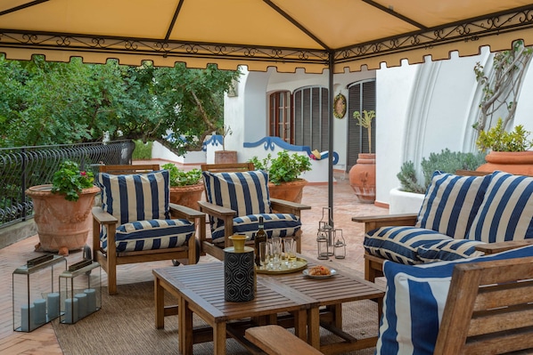 An outdoor patio with wooden furniture, striped cushions, and potted plants.