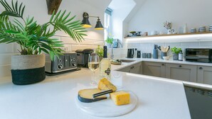 Una cocina moderna con encimera blanca, un tostador, una copa de vino y una tabla de quesos.