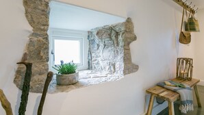 Una ventana enmarcadas en piedra con vistas al exterior, una silla de madera rústica y una cesta tejida colgada en la pared.