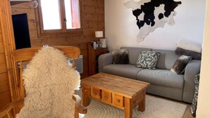 Una sala de estar acogedora con una mesa de madera, un sofá gris y un gran cuero de animal colgado en la pared.
