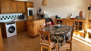 Una cocina con armarios de madera, lavadora, mesa de comedor con sillas y una lámpara colgante.
