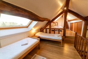 Une chambre confortable située sous les toits, avec deux lits simples, des poutres en bois, une lucarne et un petit espace bureau.