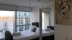 A modern hotel room with a large window, a bed with white linens, a chair, and a large artwork on the wall. - Stunning 1-bed Apartment in London With River View (London)