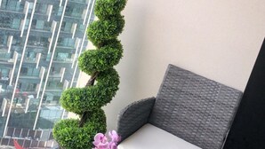 A balcony with a wicker sofa, a small table with a potted plant and a glass bowl, and a view of a modern building. - Stunning 1-bed Apartment in London With River View (London)