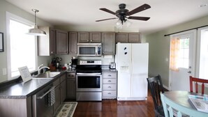 Una cocina con armarios de madera, electrodomésticos de acero inoxidable, un ventilador de techo y un comedor con mesa y sillas.