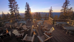 Une terrasse avec coin salon extérieur et foyer, entourée de grands arbres et offrant une vue sur la montagne.