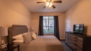 Habitación de hotel con cama, televisor, cómoda, mesita de noche y ventilador de techo.