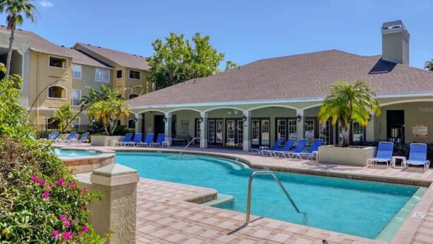 Un hotel con piscina, sillas de descanso y palmeras.