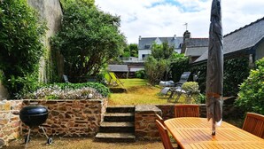 Patio con una parrilla de piedra, una mesa de madera y mobiliario exterior.