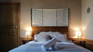 Una cama bien hecha con un cabecero estampado, dos lámparas de noche y una toalla enrollada sobre la cama.