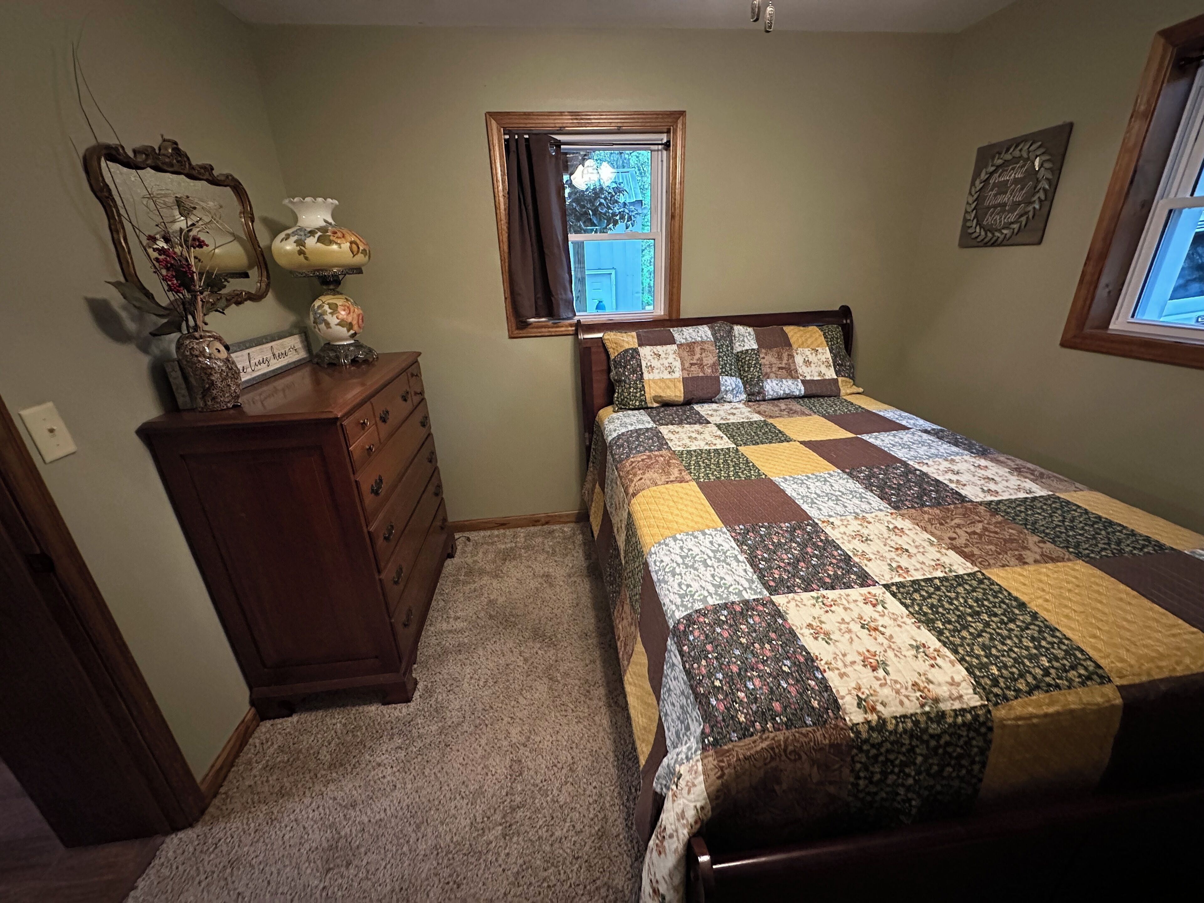 A bedroom with a wooden bed, a dresser, a mirror, and a window.