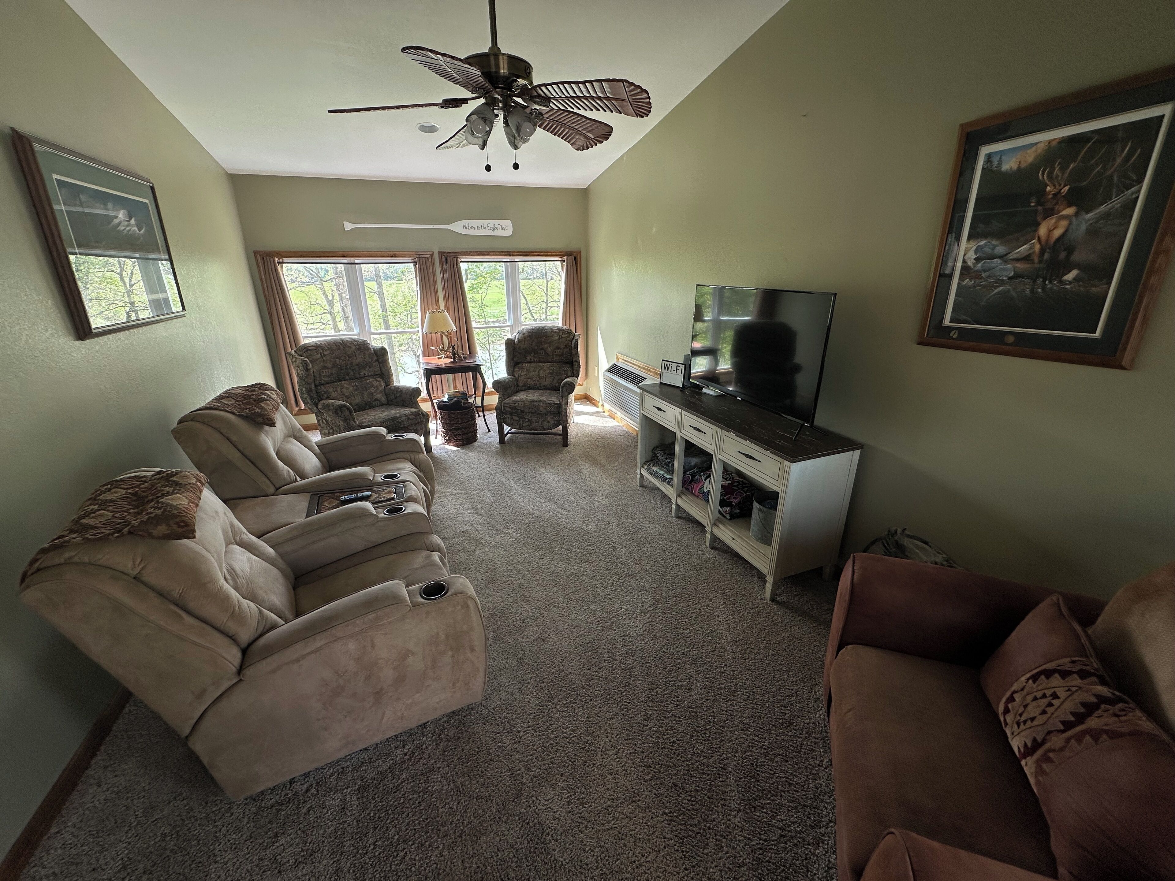 A living room with a ceiling fan, a TV on a stand, and a painting on the wall.