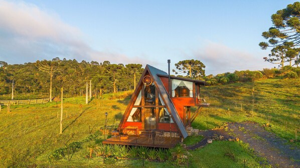 A wooden cabin with a glass front, situated on a grassy hill with a backdrop of trees. - Sítio Mar de Nuvens Chalés de Luxo (Urubici)