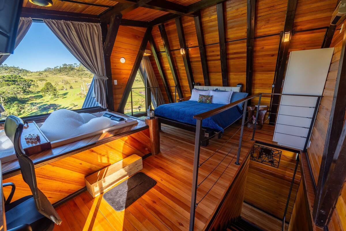 A cozy, wooden cabin bedroom with a bed, a small desk, and a view of a green landscape.