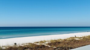 Una playa con cielo azul despejado, orilla de arena y una persona caminando por la playa.