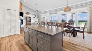Una cocina amplia con una isla grande, armarios de madera y un comedor con vista al océano.