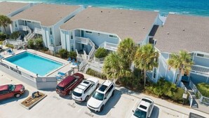 Een strandhotel met meerdere kamers, een zwembad en geparkeerde auto's.