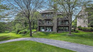 A multi-story building with a balcony, surrounded by lush greenery and a paved pathway.