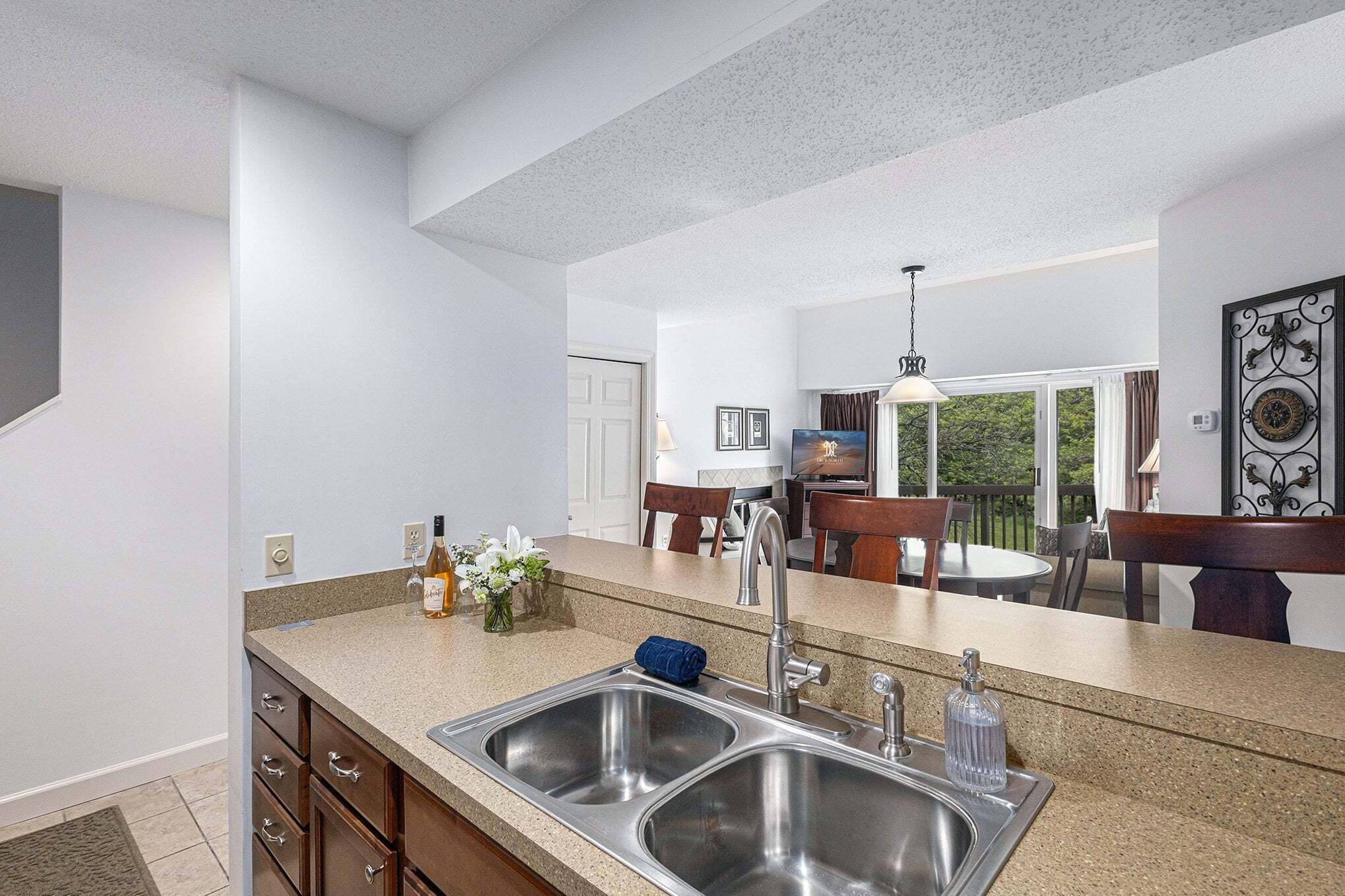 A kitchen with a double sink, a dining area with chairs, and a view of the outdoors.
