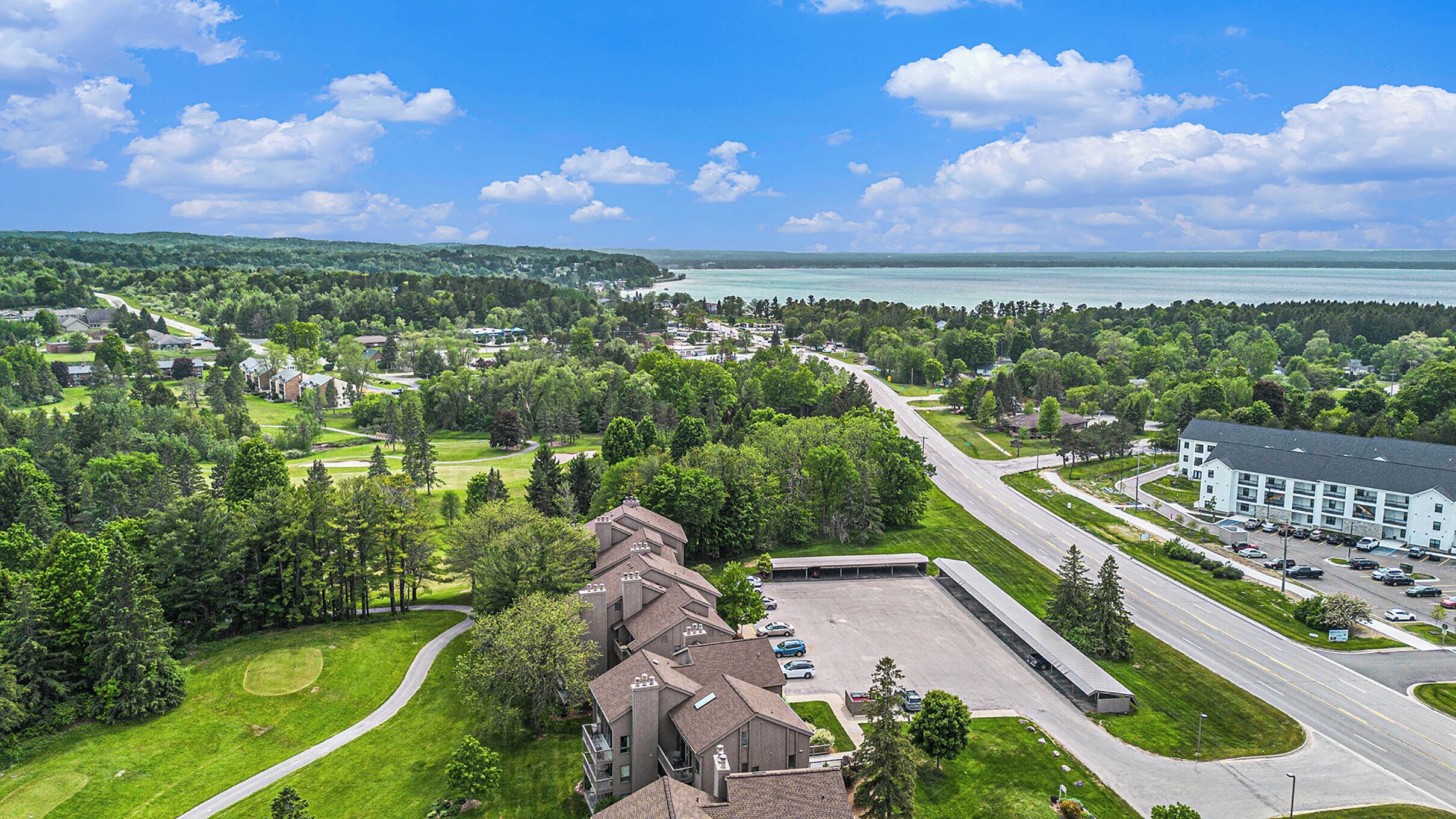 An aerial view of a residential area with a large building, roads, and a body of water in the distance.