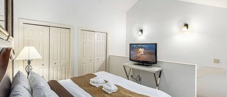 A hotel room with a bed, a television, a lamp, and a wardrobe.
