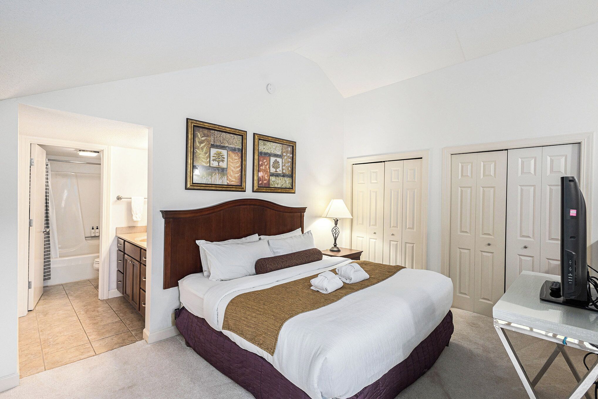 A hotel room with a bed, a desk, a TV, and a bathroom with a shower and toilet.