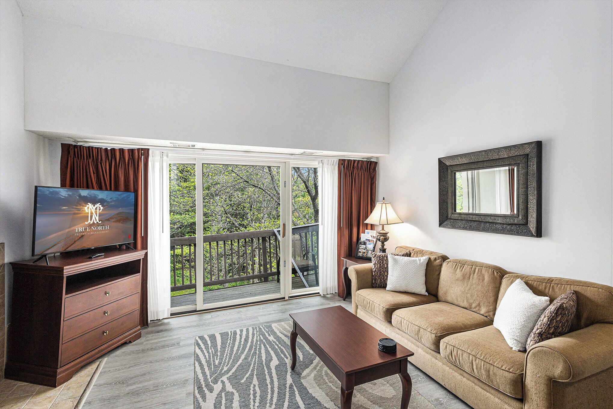 A living room with a television, a sofa, a coffee table, a lamp, and a sliding glass door leading to a balcony.