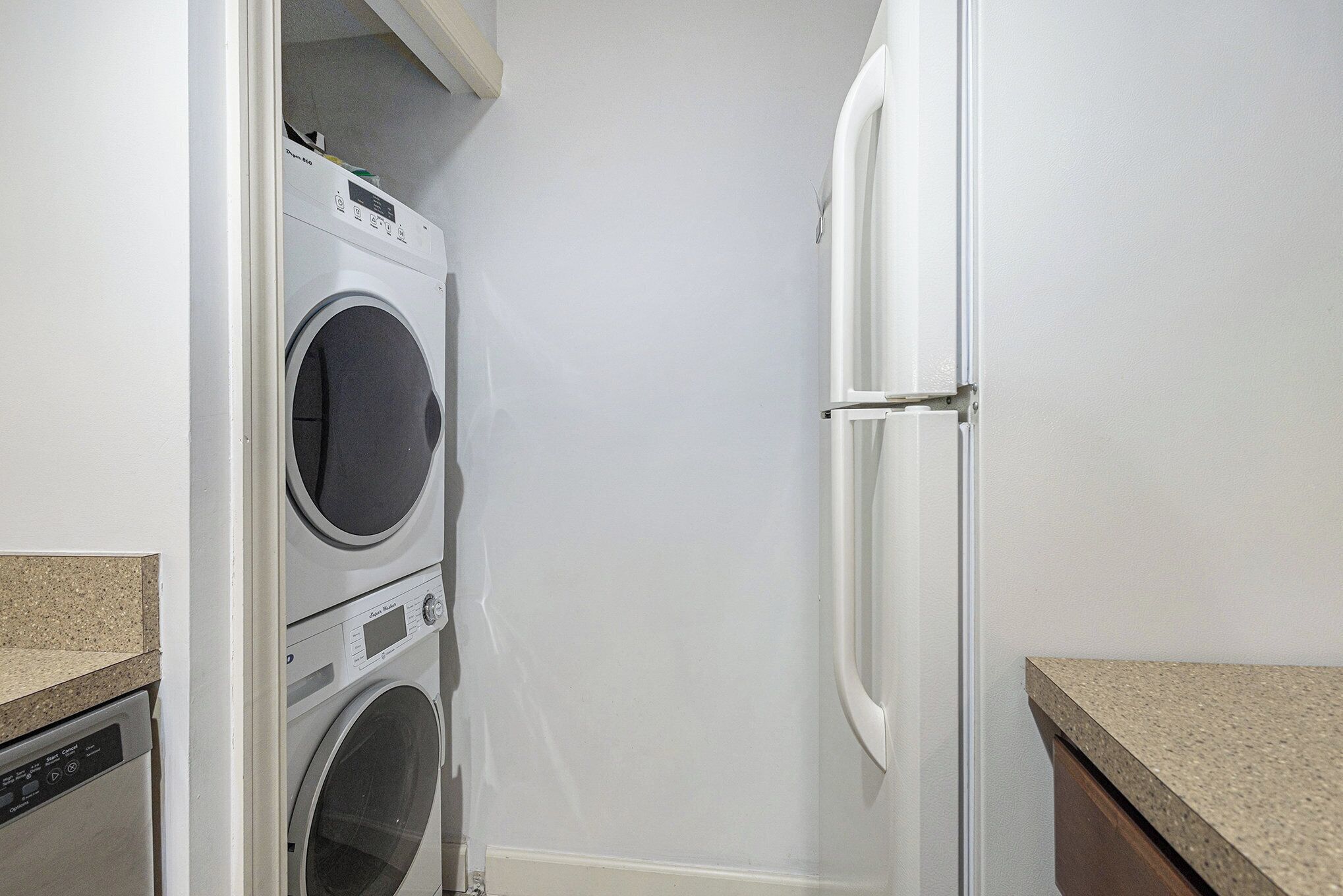 A laundry area with a stacked washer and dryer, a refrigerator, and a countertop.
