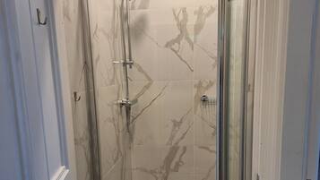 Cabina de ducha con paredes de vidrio, baldosas de mármol y puerta de metal.