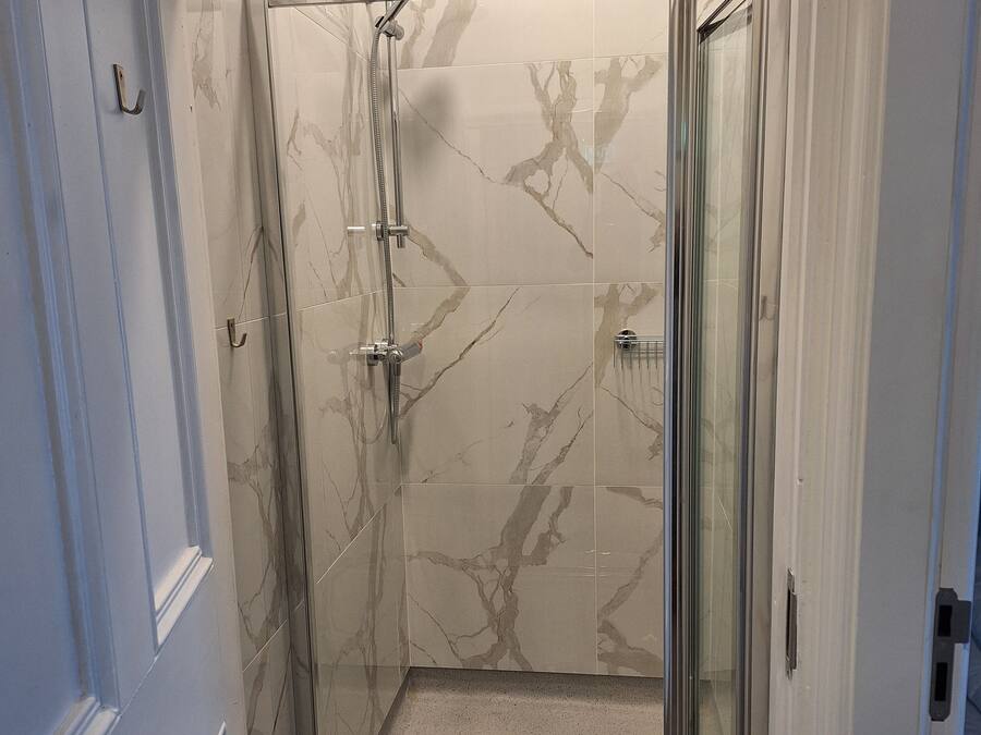 Cabina de ducha con paredes de vidrio, baldosas de mármol y puerta de metal.
