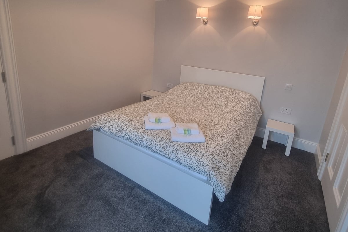 A bedroom with a bed, two bedside lamps, a nightstand, and a carpeted floor.