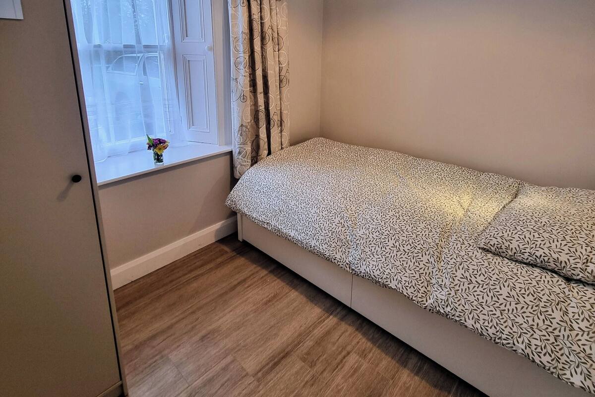 A room with a bed, a window with curtains, a door, and a ceiling light.