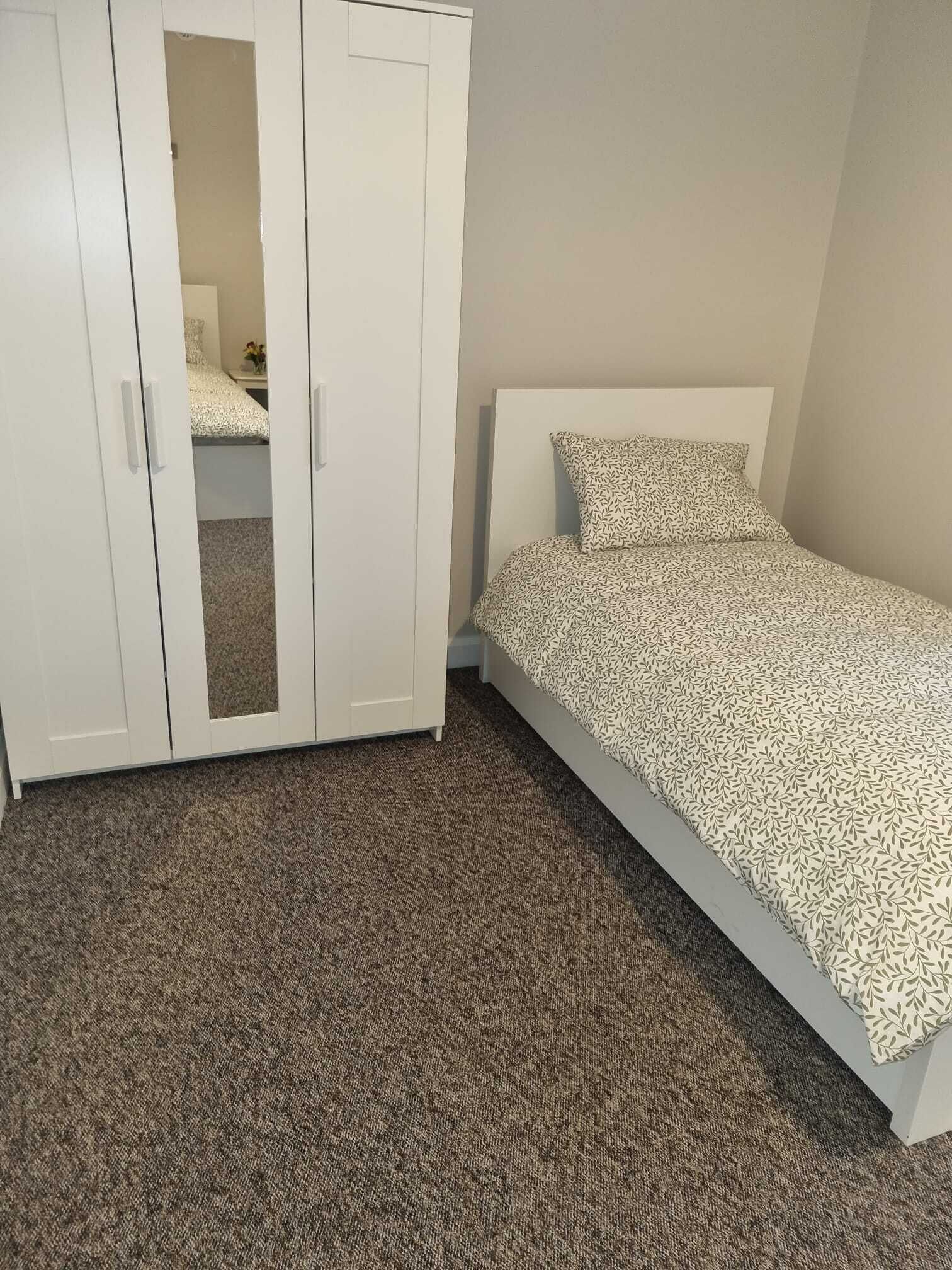 Un dormitorio con cama, un armario blanco y suelo alfombrado.
