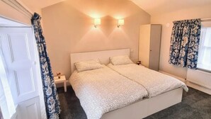 A bedroom with a large bed, two bedside lamps, a wardrobe, and a window with curtains. - The Monkey Puzzle (Bunclody)