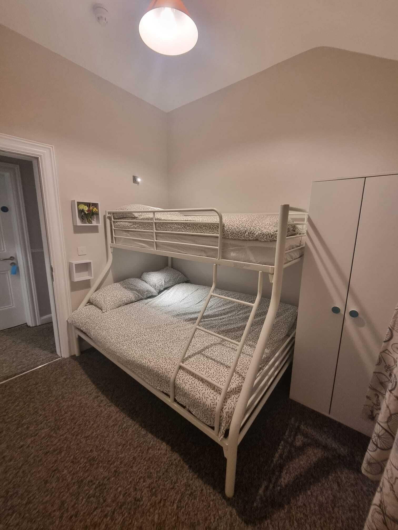 Habitación con literas, un armario y una pequeña estantería con flores, además de una puerta.