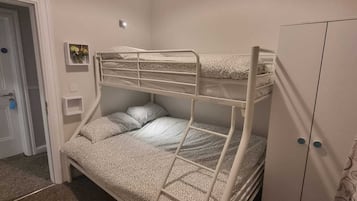 Habitación con literas, un armario y una pequeña estantería con flores, además de una puerta.