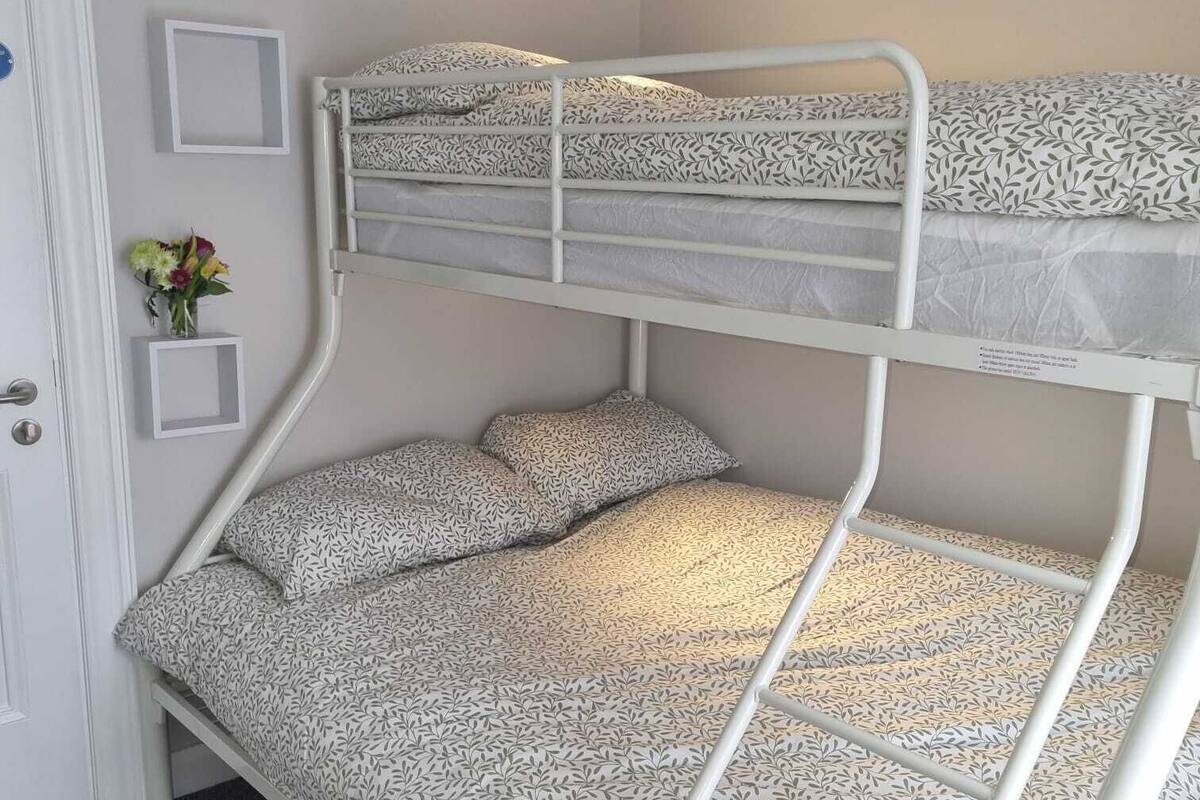 A bunk bed with patterned bedding in a room with a door, a small wall-mounted shelf, and a wall-mounted light.