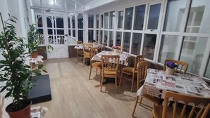 A dining area with wooden chairs and tables, large windows, and a staircase leading to an upper level. - The Monkey Puzzle (Bunclody)