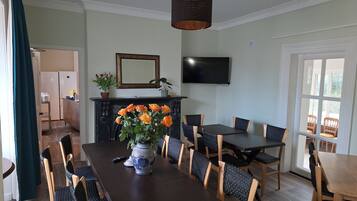 Un comedor con una mesa larga, sillas, un florero con flores, una chimenea, un televisor y un ventanal.