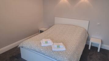 A neatly made bed with a patterned bedspread, two bedside tables, and wall-mounted lights.