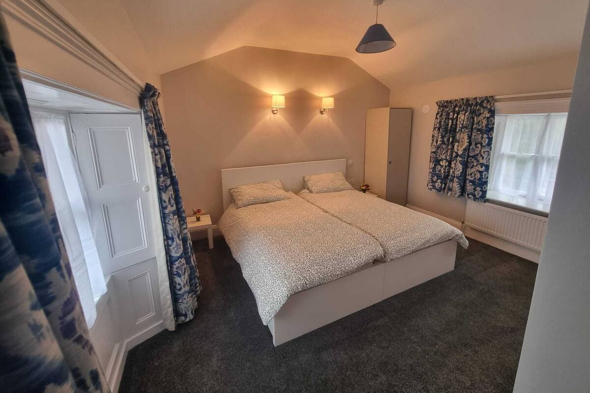 A bedroom with a large bed, two bedside lamps, a wardrobe, a window with curtains, and a ceiling light.