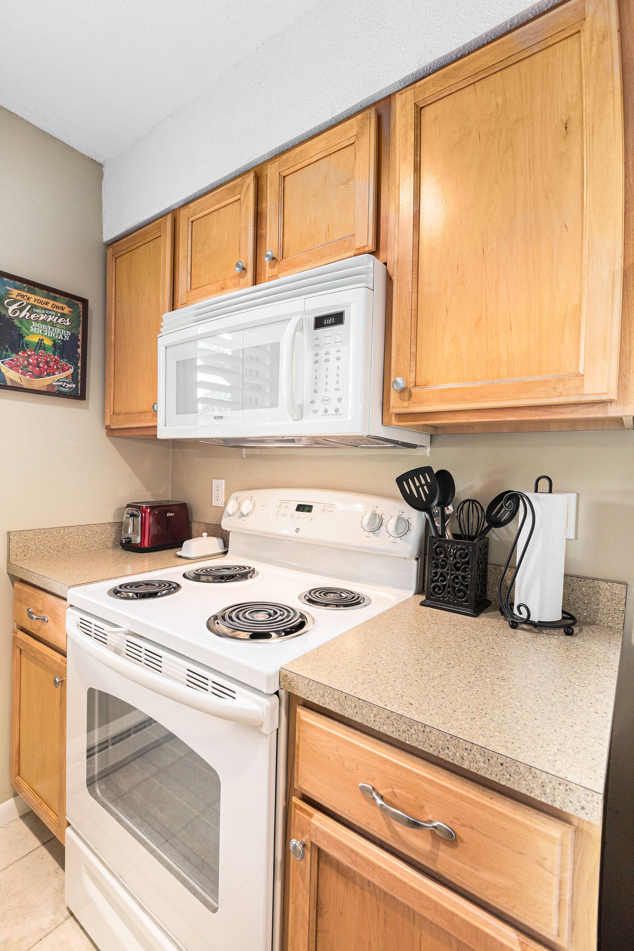 A kitchen with wooden cabinets, a white microwave, a stove, and a toaster.