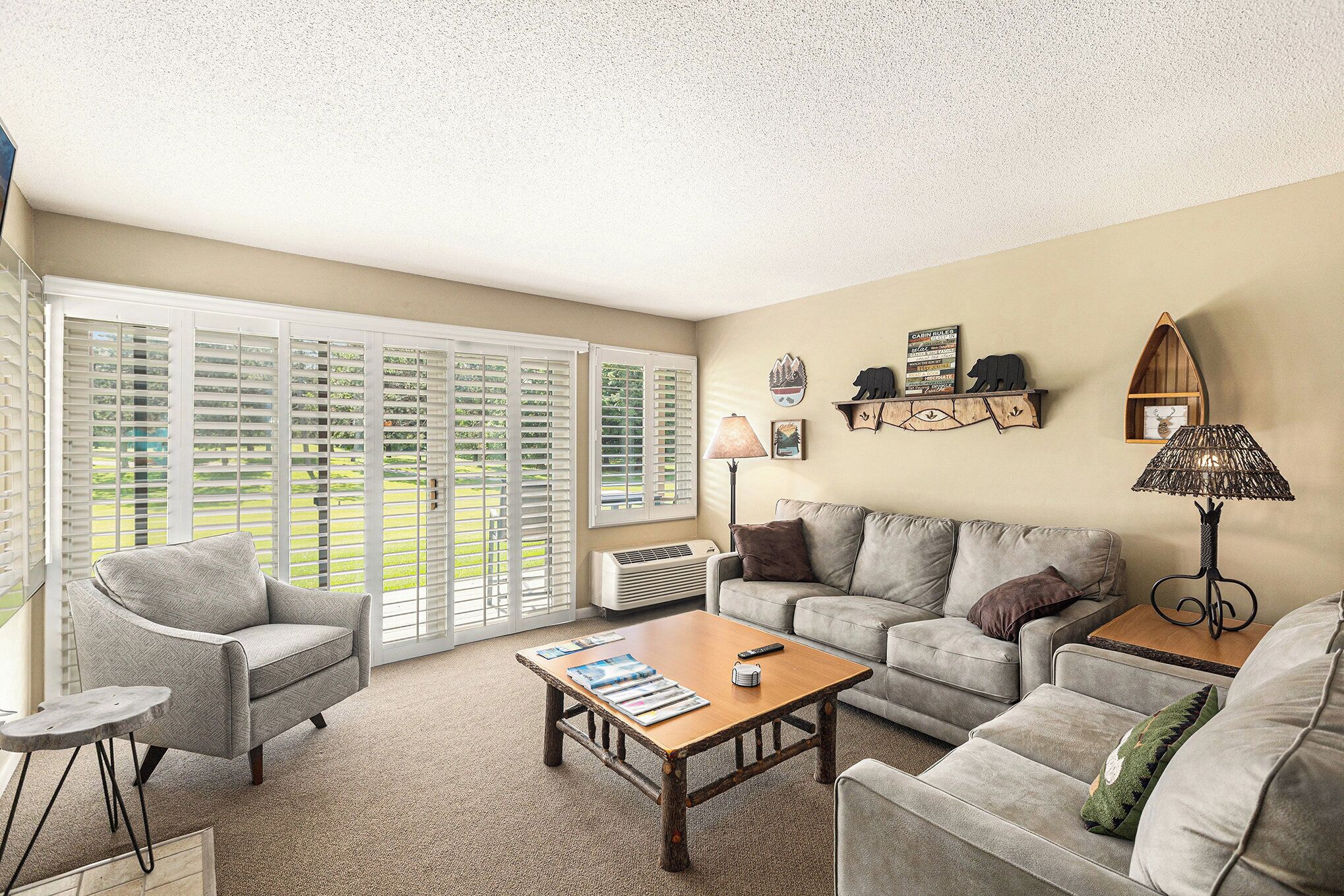 A living room with a sofa, armchair, coffee table, and a large window with blinds.