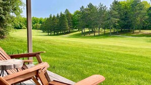 Une terrasse en bois avec deux chaises donnant sur une pelouse bien entretenue et des arbres.
