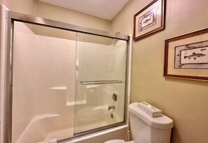 Un baño con ducha de mampara, inodoro y cuadros enmarcados en la pared.
