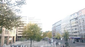 A street view with modern buildings, a tree-lined sidewalk, and a clear sky. - Mainhouse  (Düsseldorf)