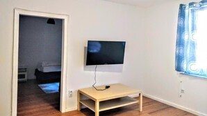 A room with a television mounted on the wall, a small wooden table, and a window with blue curtains. - Mainhouse  (Düsseldorf)
