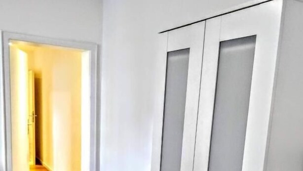 A room with a wooden floor, white walls, and a white wardrobe with two doors. - Mainhouse  (Düsseldorf)