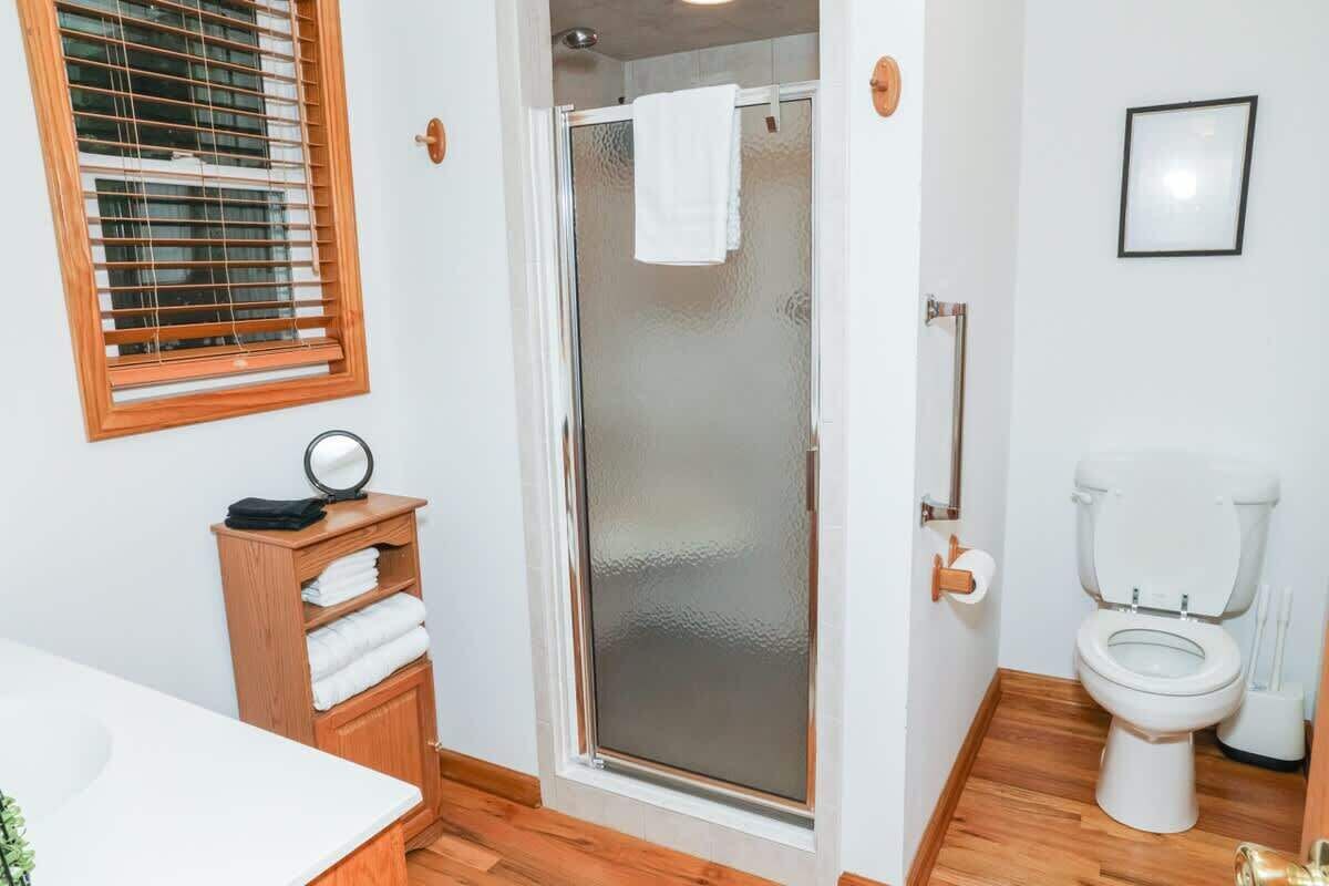 A bathroom with a glass shower enclosure, a wooden vanity with a mirror, a toilet, and a framed picture on the wall.