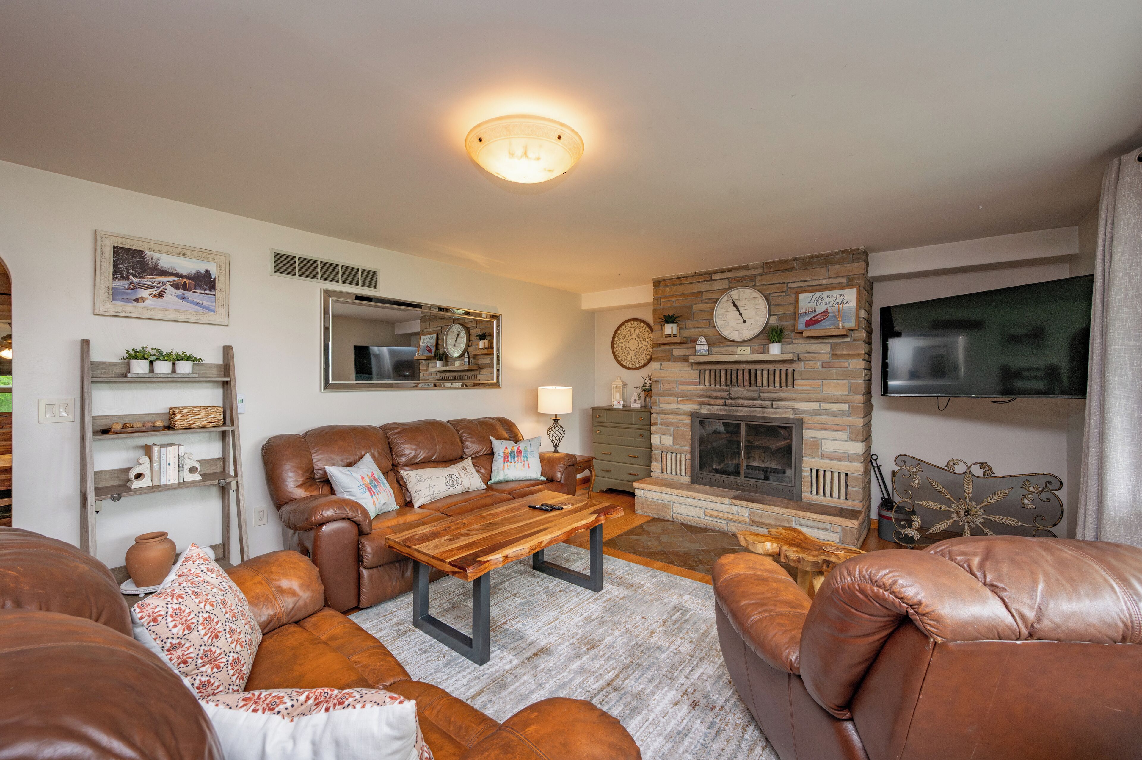 A cozy living room with leather sofas, a wooden coffee table, a fireplace, and a television mounted on the wall.